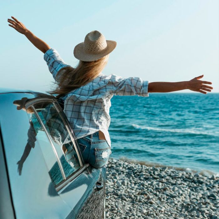Mujer disfrutando brisa marina desde coche junto al mar y de su desconexión digital.